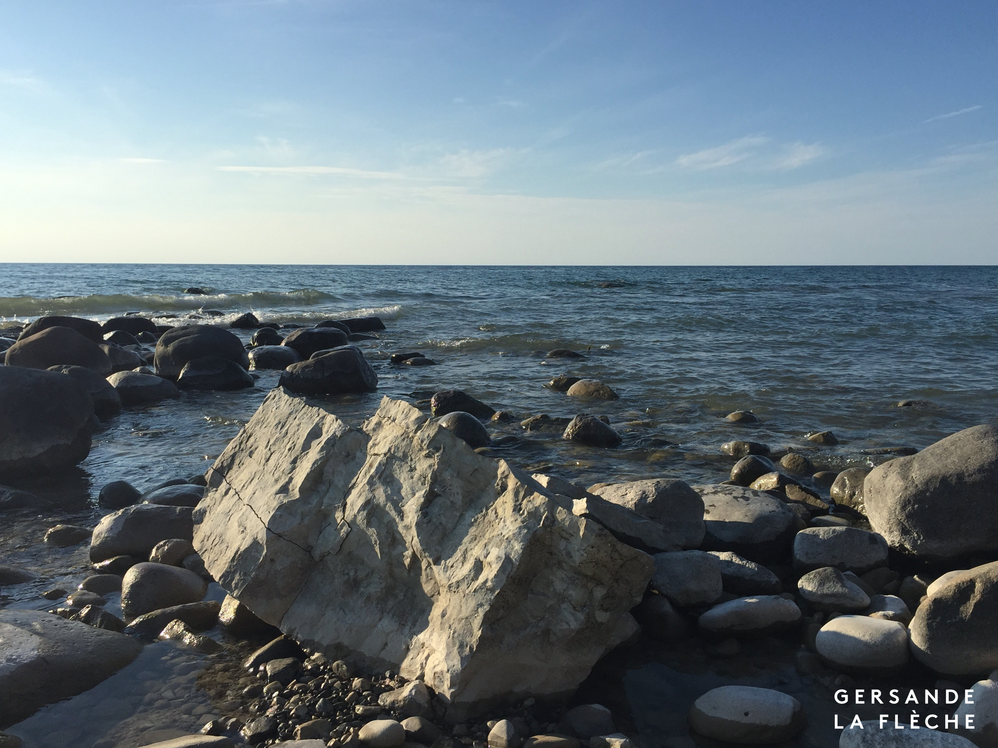 A picture of grey rocks jutting out of a lake, the water is calm and the sky is bright.