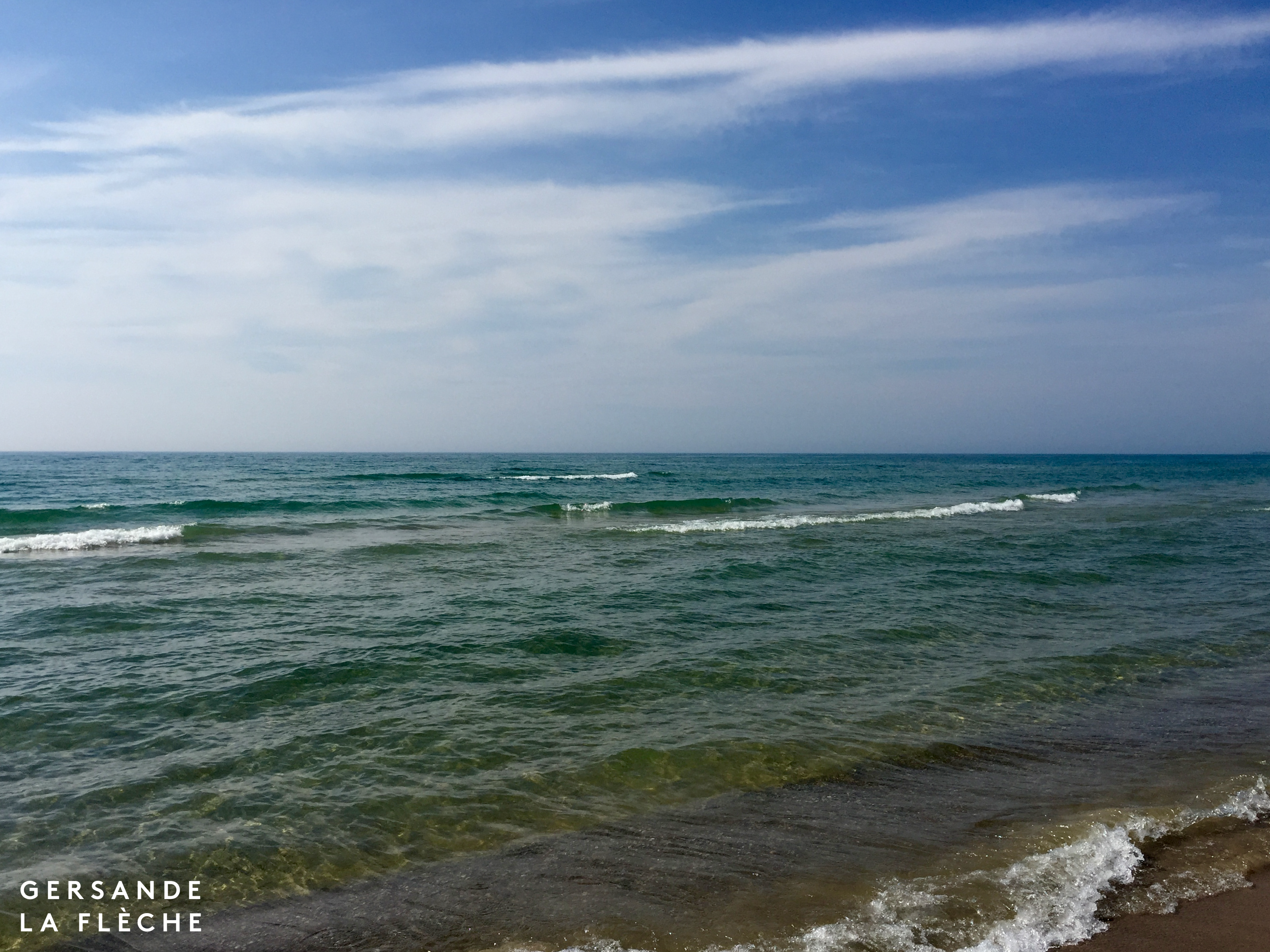 A picture of a blue sky, and the horizon of a immense lake, turquoise water that is also stunningly clear rolls into small waves as they reach the shore.