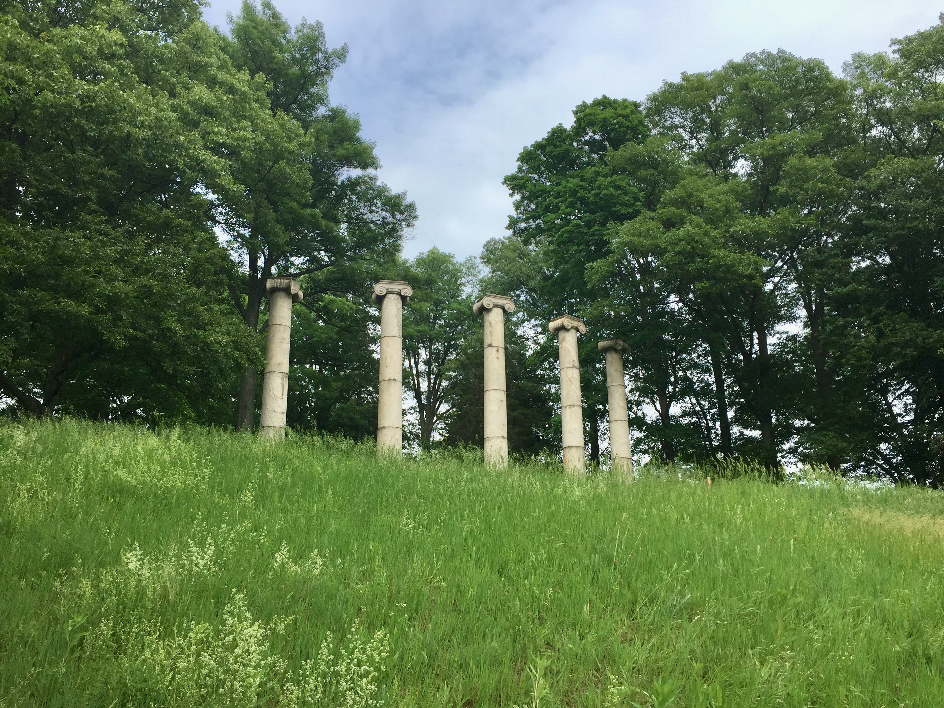 Several colums at the top of a hill, surrounded by trees.