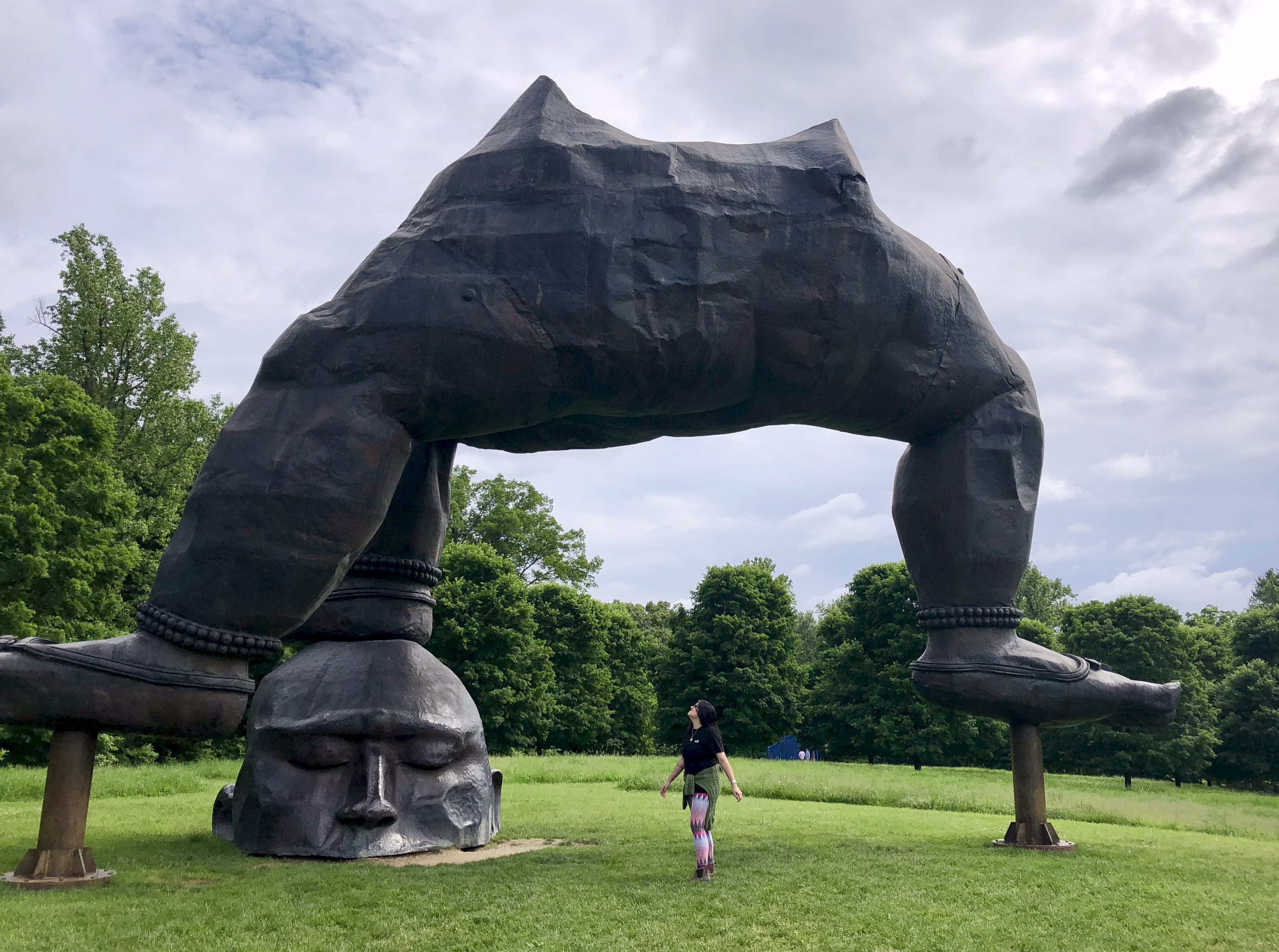 A photo of Gersande standing underneath the huge sculpture of the Three Legged Buddha by Zhang Huan.