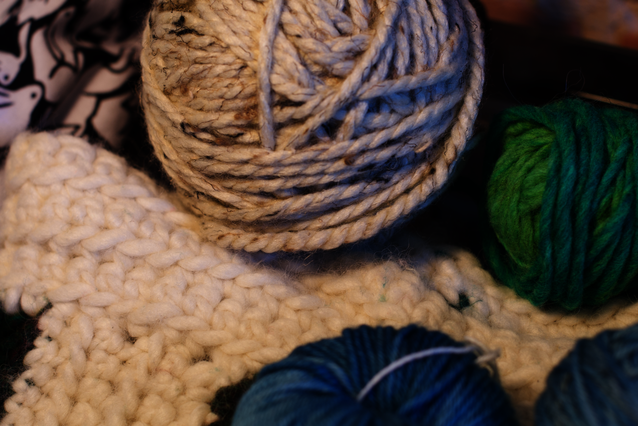 An aesthetically-pleasing photo of some green, blue, and grey balls of yarn on top of a white and green neckwarmer I made last fall. 