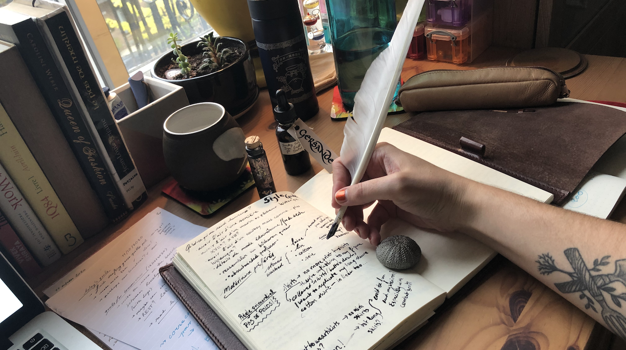 A photo of my journal where I wrote with a goose quill and iron gall ink. I'm holding the white goose in my hand. 