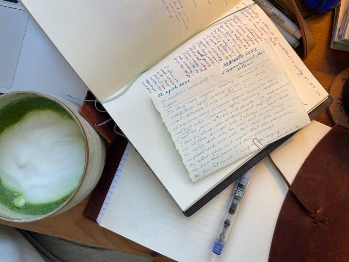 Papers strewn about on my desk, a cup of a matcha latte in the corner of the photo.