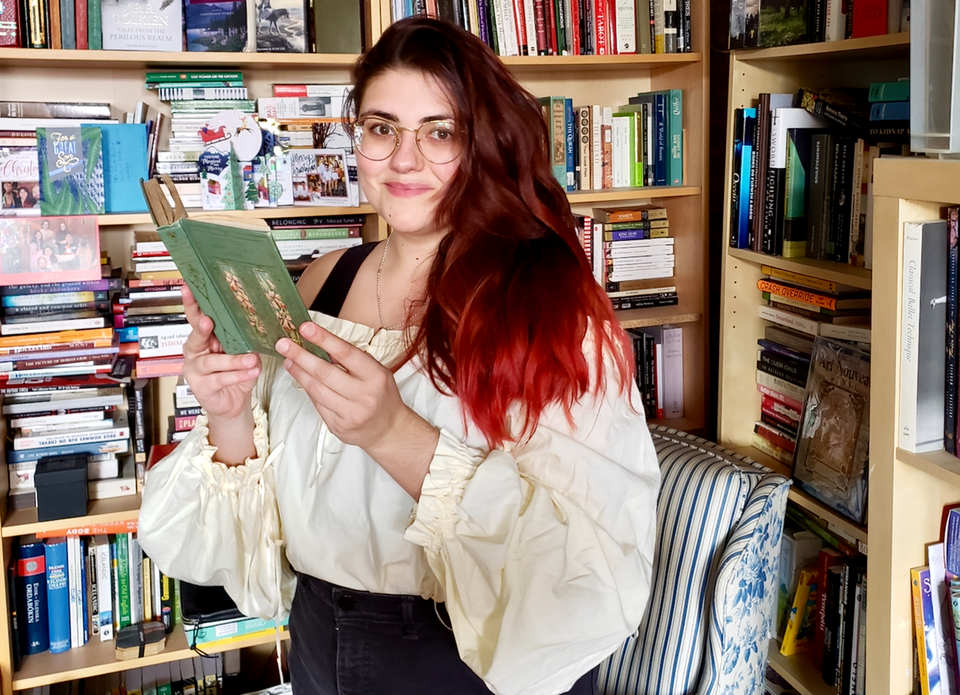 A photo of Gersande in front of a bunch of bookshelves and wearing a very fluffy cotton shirt, a historical reproduction.
