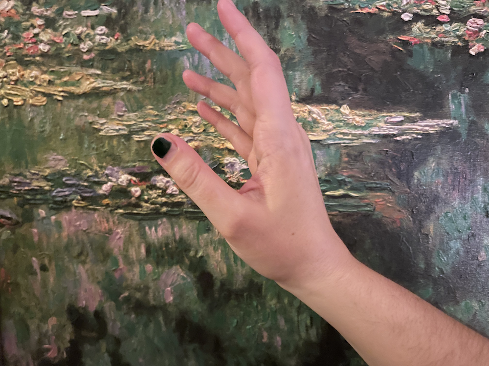 A photo of my hand in front of a reproduction of a Monet painting.