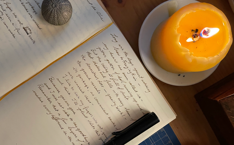 An image of a candle, and a notebook, open to a page with my handwriting of one of my NaPoWriMo drafts.