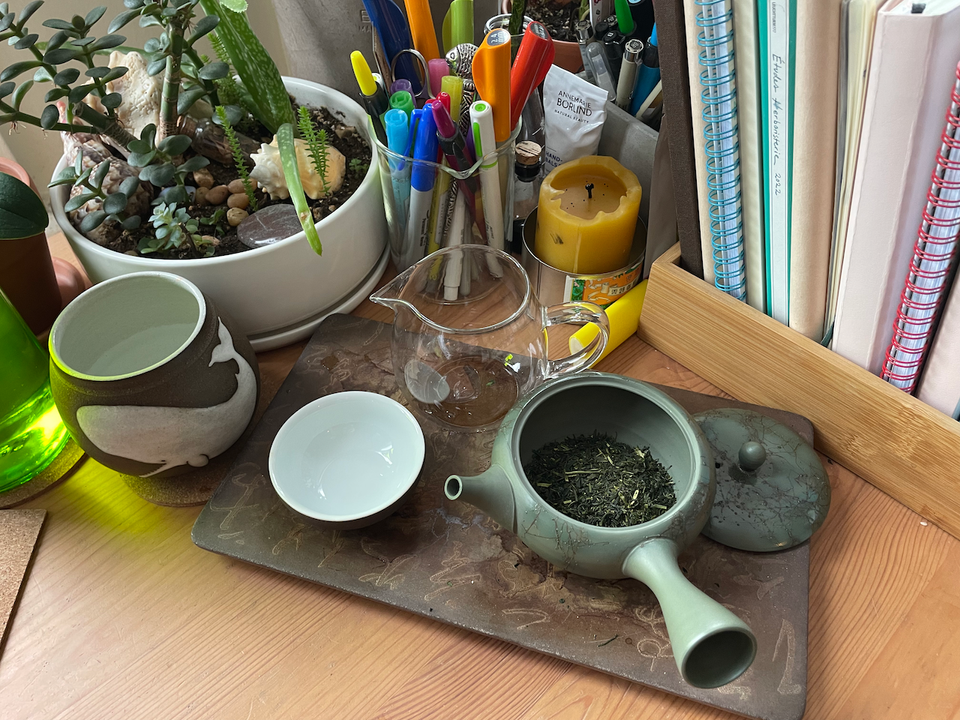 A corner of my desk featuring a tea tray, succulents, a glass of water, too many notebooks, and many markers and pens.